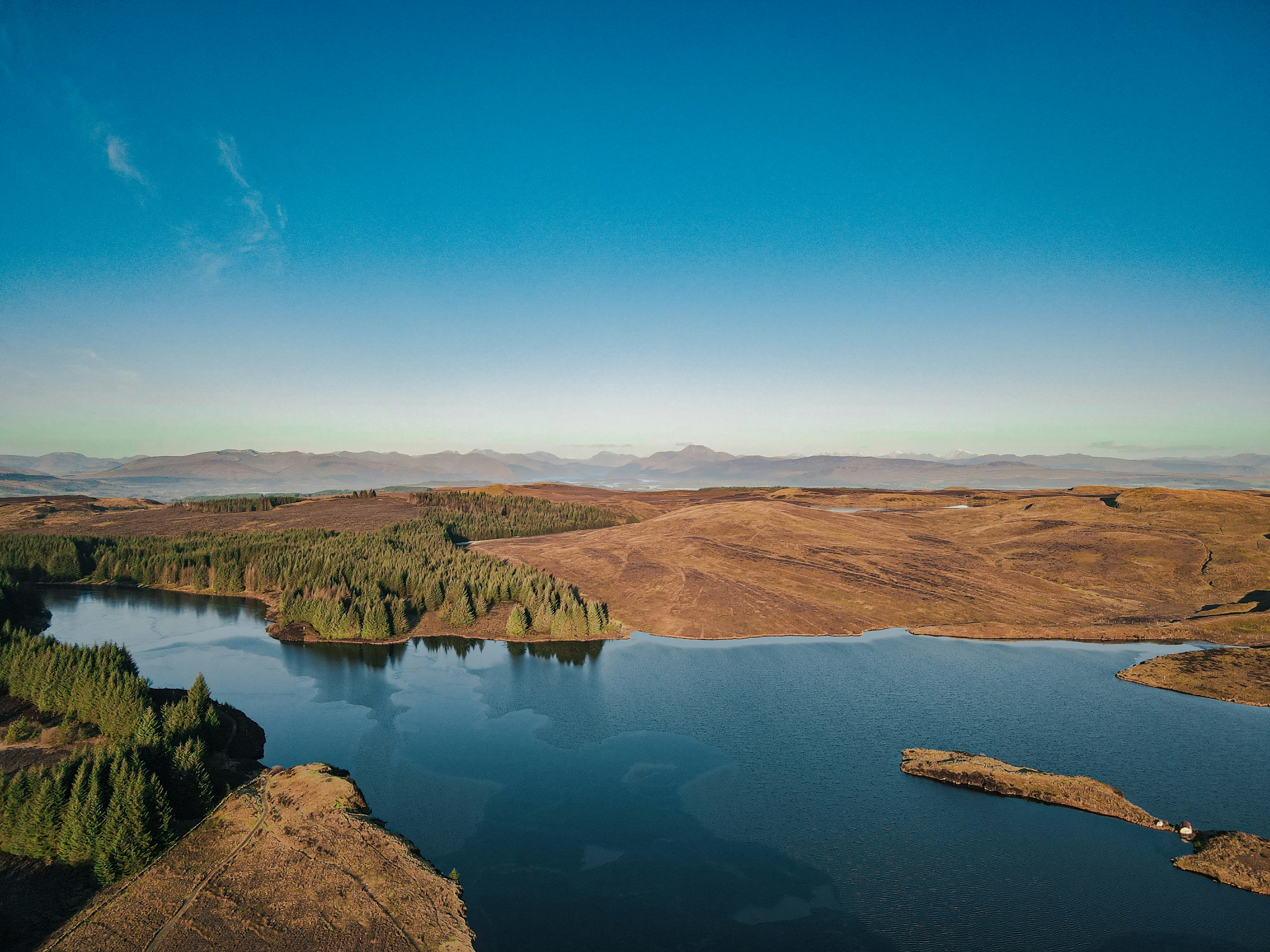 brown mountains near lake under blue sky during daytime